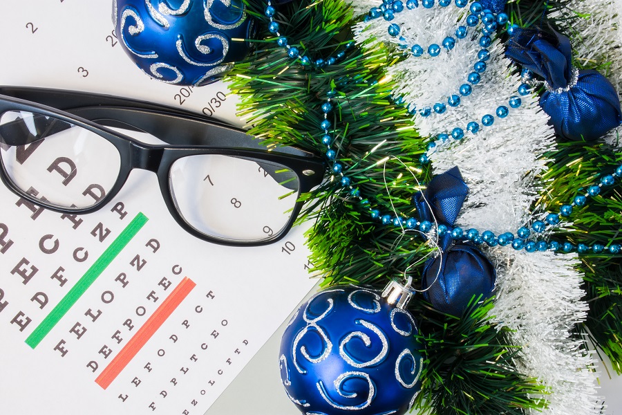 Ophthalmology or optometry Christmas and New Year with decorations. Eyeglasses and table for measure visual acuity lying near artificial snow with glitter, toys and blue balls on Christmas tree Improve your vision during the Holidays with LASIK.